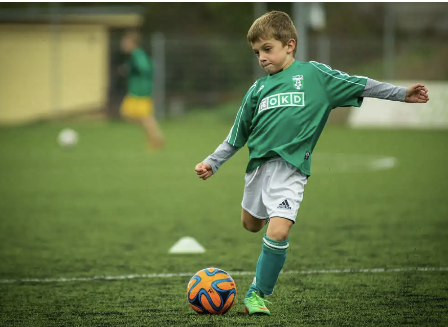 Young football player in green jersey practicing ball control and dribbling skills during training