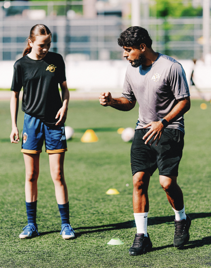 Soccer coach providing one-on-one technique instruction to young player on training field